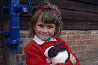 ENGLAND, Hampshire, Andover, Young girl holding a black and white rabbit at Finkley Down Farm