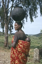 BURUNDI, People, Hutu woman carrying baby in sling on her back and water pot on her head