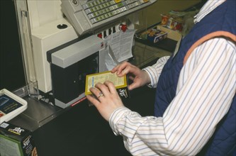 SHOPS, Supermarket, Interior, Cashier swiping item across electronic barcode reader at till.