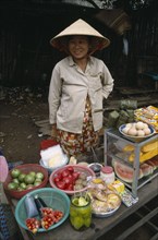 VIETNAM, South, Saigon, Smiling woman wearing traditional conical hat selling fruit and vegetables