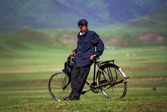 CHINA, Gansu, Xiahe, Weary traveller leaning against bicycle in green landscape