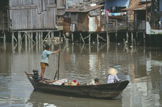 VIETNAM, South, Saigon, Man rowing boat past waterside houses on the Kinh Ben Nghe a tributary of