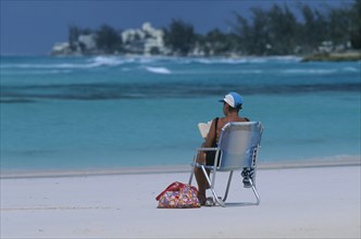 WEST INDIES, Barbados, Worthing, Woman sitting in a deck chair reading on Sandy Beach