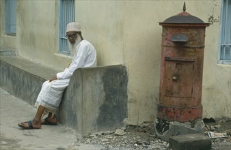 TANZANIA, Zanzibar Island, Elderly Muslim man sitting at roadside beside post box.