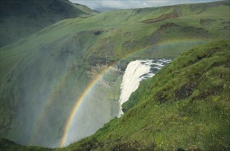 ICELAND, Skogafoss, View of the waterfall and lush green surroundings with rainbow
