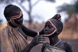 SUDAN, Tribal People, Dinka girl decorating the face of a friend using dung ash mixed with water or