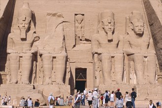 EGYPT, Nile Valley, Abu Simbel, Sun Temple of Ramses II.  Tourists at entrance flanked by four