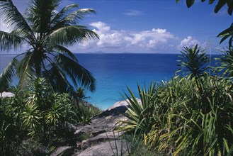 SEYCHELLES, Fregate Island, View through rocks and foliage toward the turquoise sea with islands of
