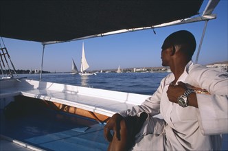 EGYPT, Nile Valley, Aswan, Cropped view of man on board felucca looking across water towards others