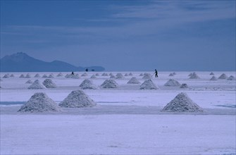 BOLIVIA, Altiplano, Salar de Uyuni, View over the salt plains with figure sweeping up piles of salt