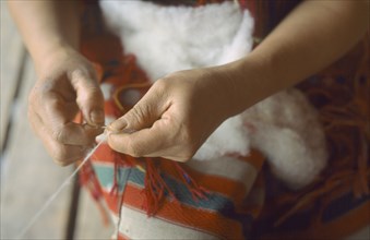 THAILAND, Huay Hom, Member of Karen tribe spinning wool by hand.  Cropped view of hands and yarn.