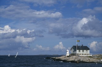 SWEDEN, West Coast, Headland with small building and lighthouse and passing sailboats