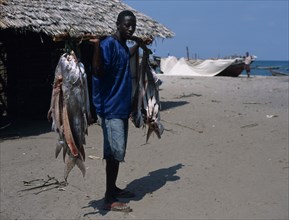 TANZANIA, Pangani, Fisherman standing on the beach with some of his days catch