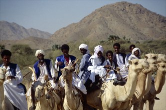 ERITREA, Nomadic People, Nomads riding camels on road between keren and Agordat with backdrop of