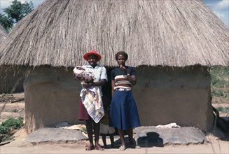 ZIMBABWE, General, Young Shona women and children standing outside thatched hut.