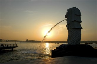 SINGAPORE, Merlion, Merlion statue spouting water in silhouette overlooking Singapore River at