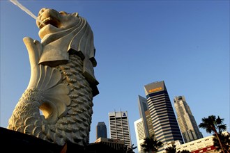 SINGAPORE, Merlion, Merlion statue spouting water in evening light with city skyscrapers beyond