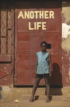 UGANDA, Kampala, Young boy standing by a red door under the words Another Life
