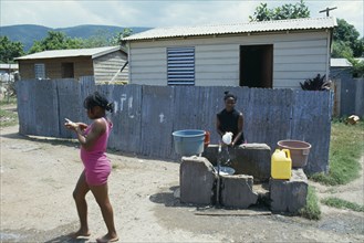 WEST INDIES, Jamaica, Kingston, Bower Bank Transit Camp.  Girls beside water pipe with simple