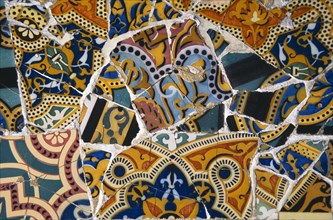SPAIN, Catalonia, Barcelona, Parc Guell.  Detail of colourful mosaic by Gaudi from a park bench