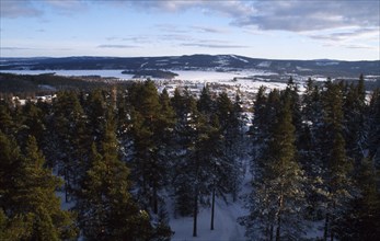 SWEDEN, Kooparberg, Leksand, Snow covered landscape with pine trees and distant town