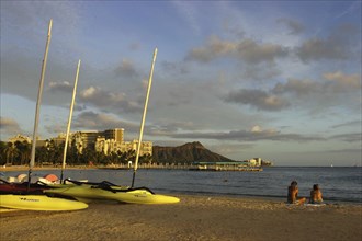 USA, Hawaii, Honolulu, Diamond Head. Sandy beach with two people sitting near boats on the sand in