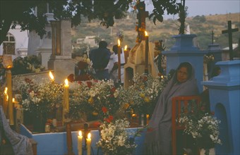 MEXICO, Puebla, Acatlan, Woman keeping vigil beside grave decorated with candles and flowers during