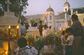MEXICO, Puebla, Acatlan, People keeping vigil beside graves decorated with candles and flowers