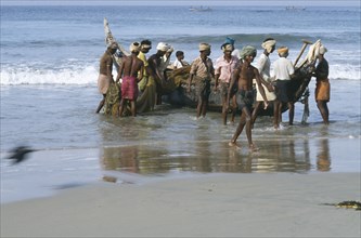 INDIA, Kerala, Kovalam Beach, Fisherman dragging boat from the sea on to beach.