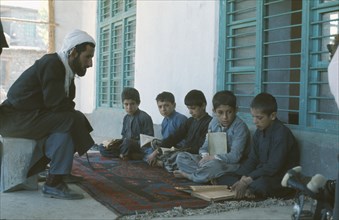 IRAN, Baluchi, Boys seated on carpet at Koranic school being instructed in the scriptures.