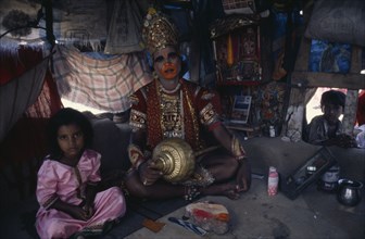 INDIA, Gujarat, Bhavnagar, Man in his shanty house dressed up as the Hindu deity Hanuman.  Child