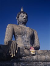 THAILAND, North, Sukhothai Province, Wat Mahathat. Seated Buddha statue holding pink ribbon flower