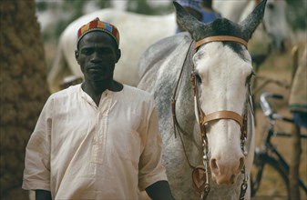 NIGERIA, Katsina, Man walking beside horse.