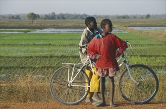 BURKINA FASO, Bobo Dioulassou, Two boys with a bicycle with paddy field behind.