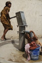 INDIA, Rajasthan, Amber, Children filling bucket and drinking from Tara water pump