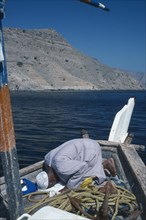 OMAN, Musandum, Fisherman praying on deck of boat.