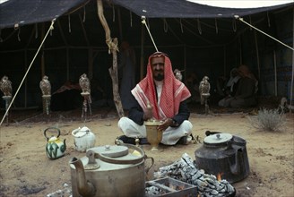 MIDDLE EAST, Bedouin, Bedouin man sitting outside his tent with row of pirched falcons behind him
