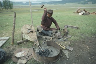 MONGOLIA, North, Sishhed Valley, Blacksmith using bellows to fan fire whilst hammering metal