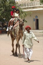 INDIA, Rajasthan, Jaipur, Man leading camel with three children riding on its back