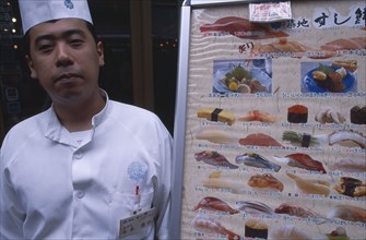 JAPAN, Honshu, Tokyo, Tsukiji Fish Market with chef standing beside seafood menu board