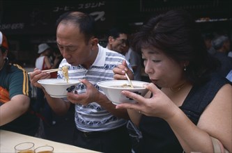 JAPAN, Honshu, Tokyo, Tsukiji Fish Market. People eating with chopsticks at noodle stall