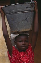 GHANA, People Carrying Goods, Portrait of child carrying large metal pail of water on her head.