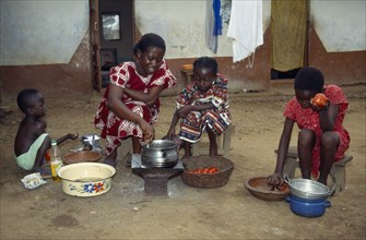 GHANA, Cooking, Woman with children cooking Abenkwan or palm nut soup a thick broth made from the