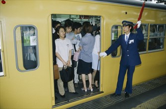 JAPAN, Honshu, Tokyo, Commuters in packed train with guard about to close doors.