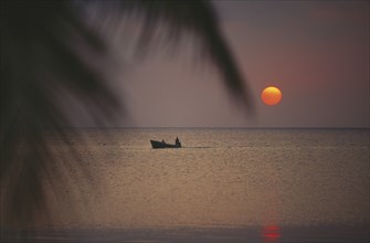 HONDURAS, Bay Islands, Roatan, Sunset seen from the beach with passing boat in silhouette and