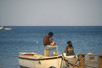 HONDURAS, Bay Islands, Roatan, Local couple with a baby sitting on wooden jetty at West End with