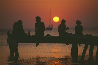 HONDURAS, Bay Islands, Roatan, Tourists sitting on jetty at West End silhouetted against warm