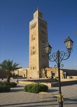 MOROCCO, Marrakech, Koutoubia Mosque tower seen from pavement with blue sky behind and street lamps