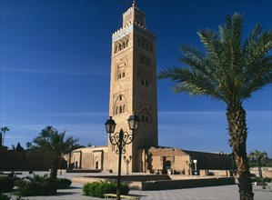 MOROCCO, Marrakech, Koutoubia Mosque tower seen from pavement with blue sky behind and palm trees