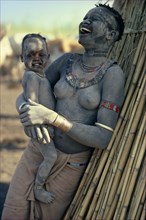 SUDAN, Mundari, "Agar Dinka woman decorated with dust, holding young son in her arms and laughing.